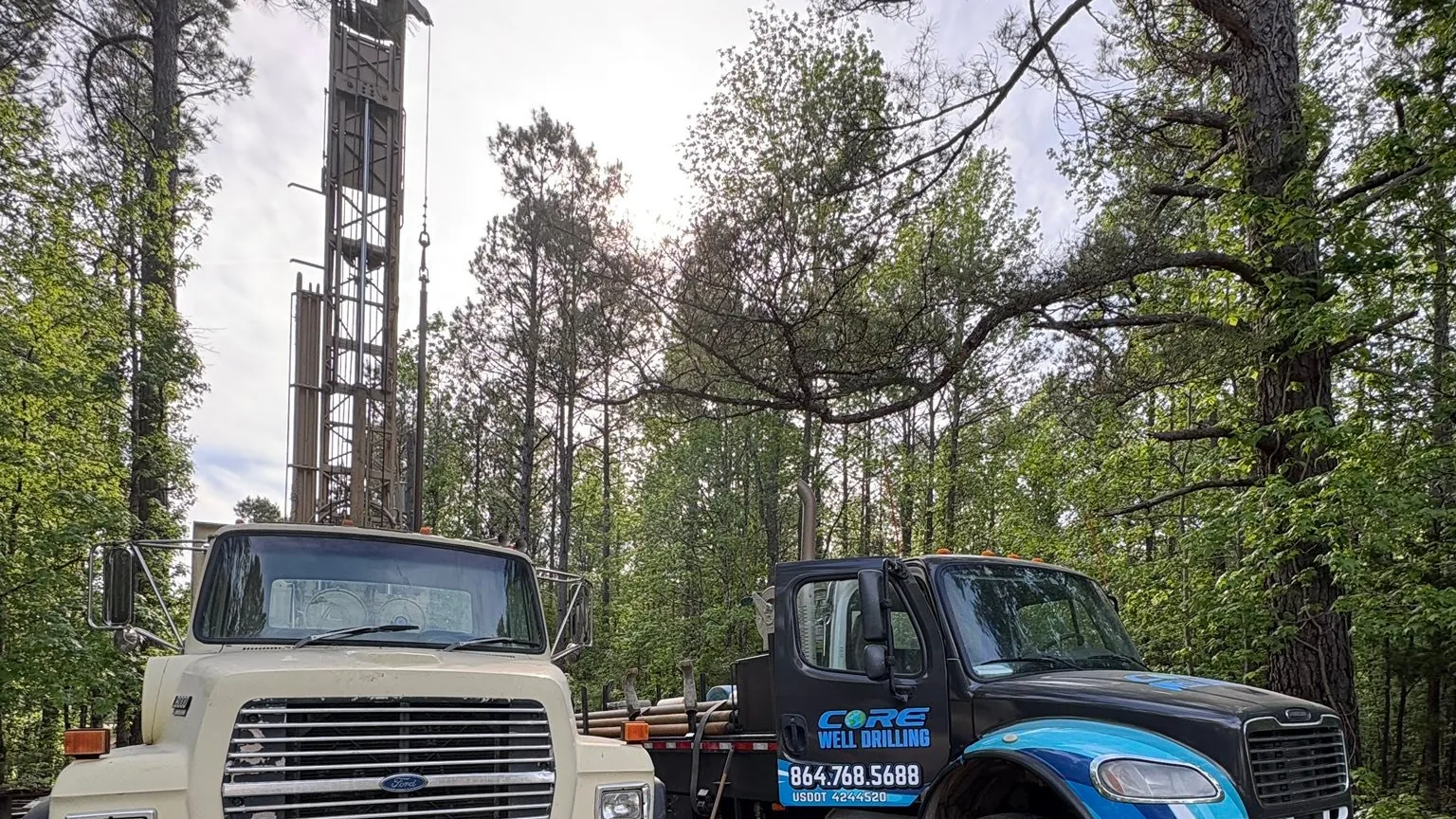 The water tank truck and the wrapped drilling truck parked together on a wooded lane