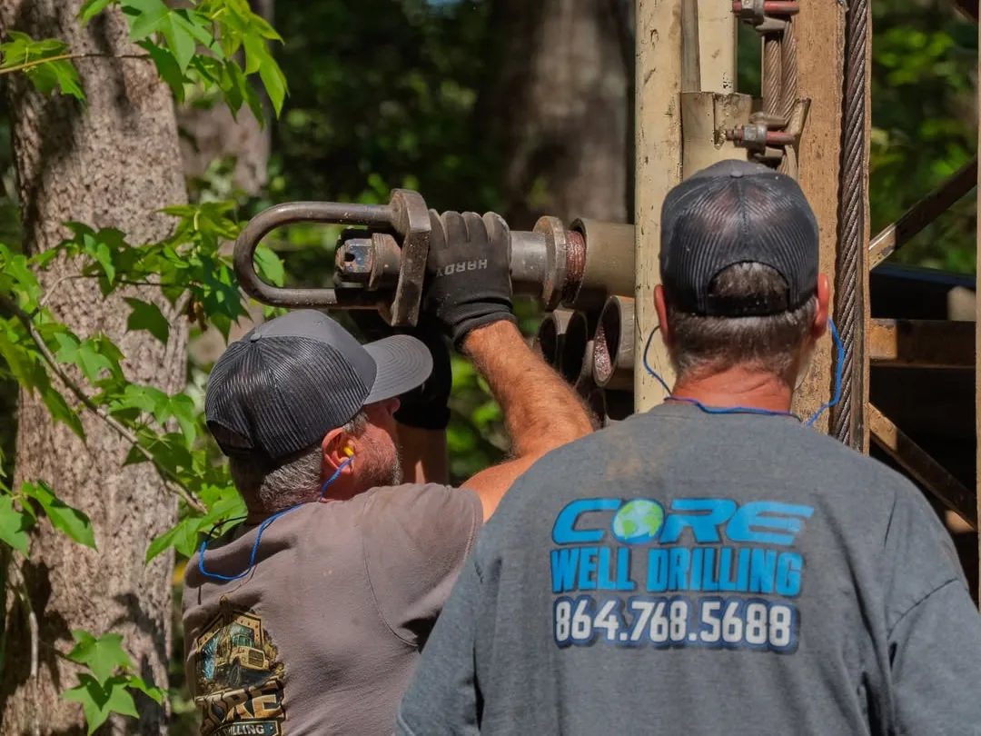 Two crew members in Core Well Drilling shirts guiding the drill head at the rig