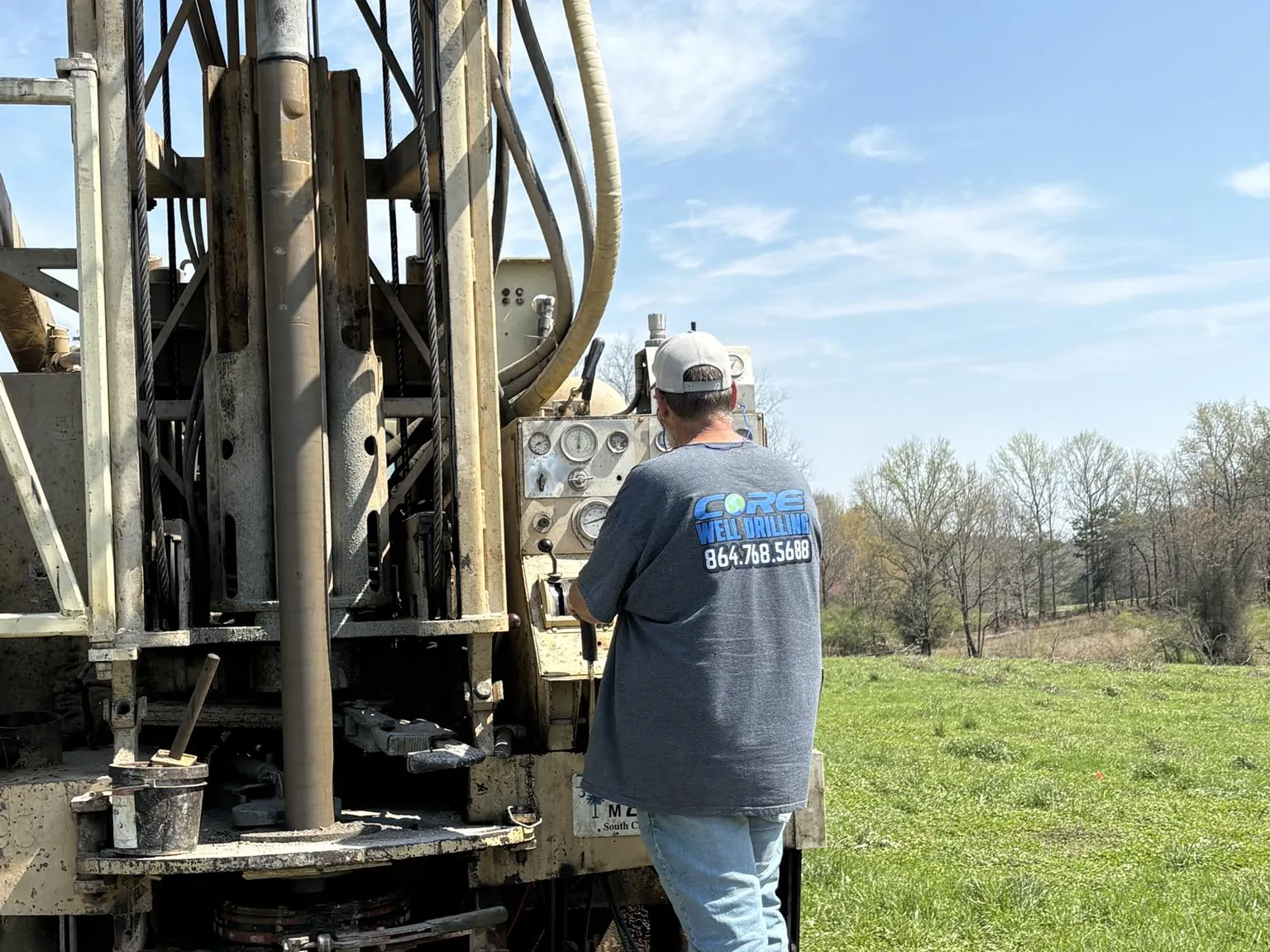 A drill rig set up in an open green pasture with a discharge pipe running out across the field