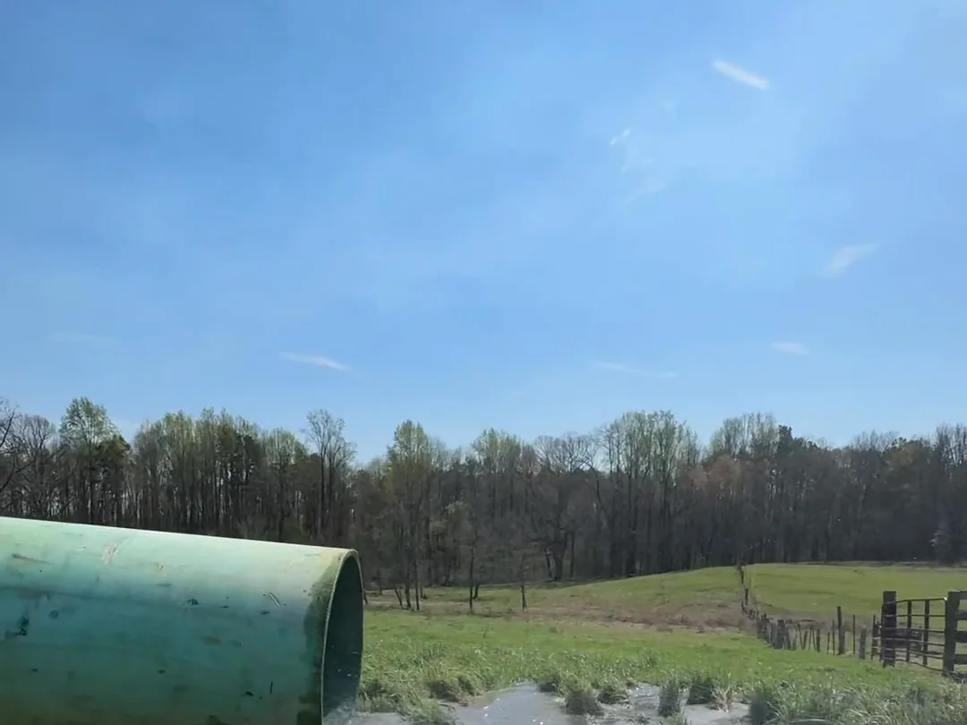 A large green discharge pipe pouring well water out across an open pasture