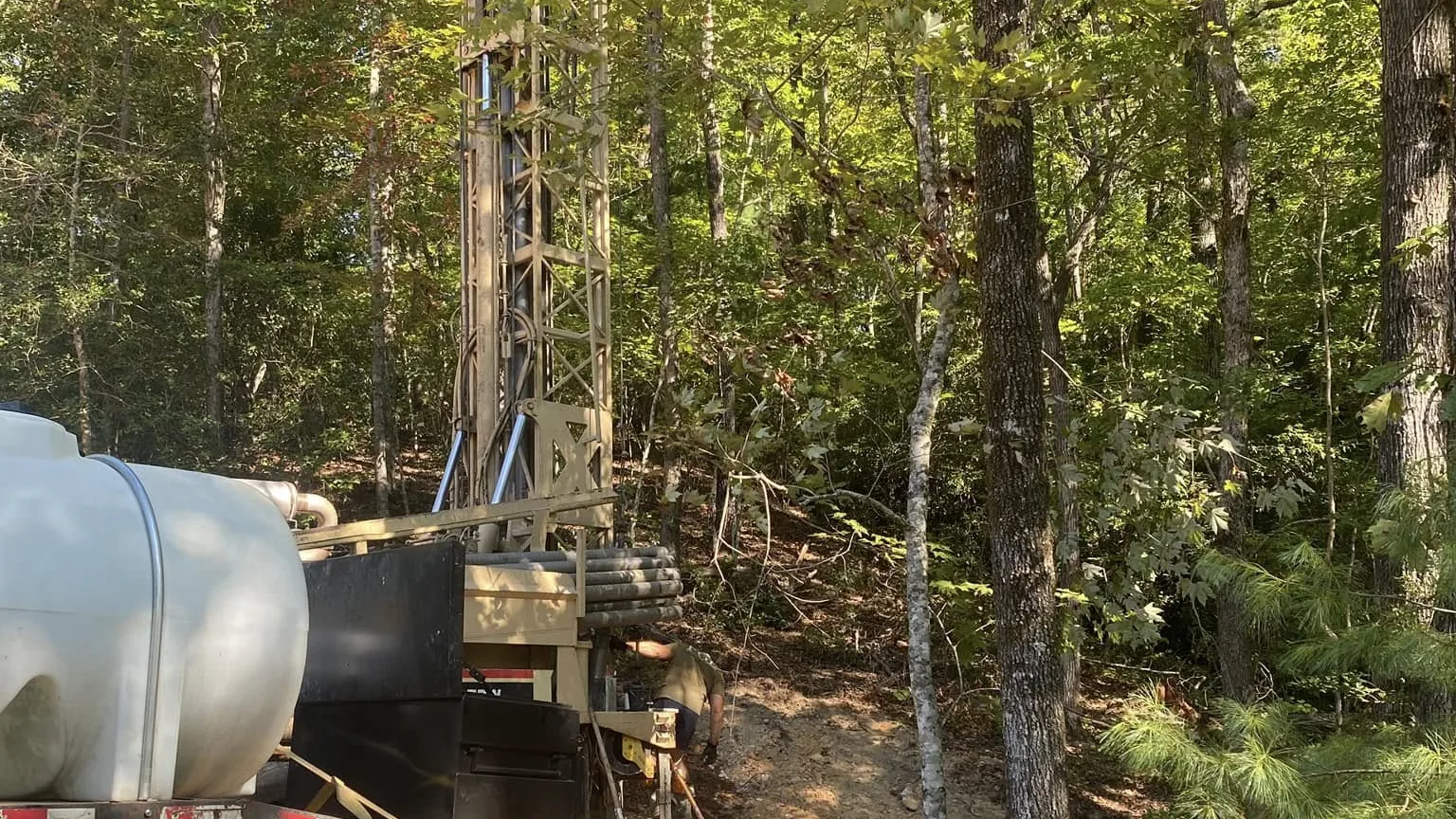 The company's water tank truck and drill rig staged together on a wooded job site