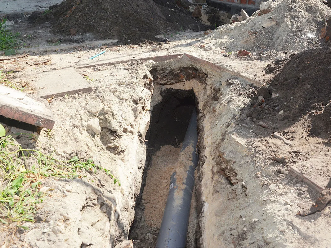 A black water line bedded on sand in the bottom of an open trench beside a walkway