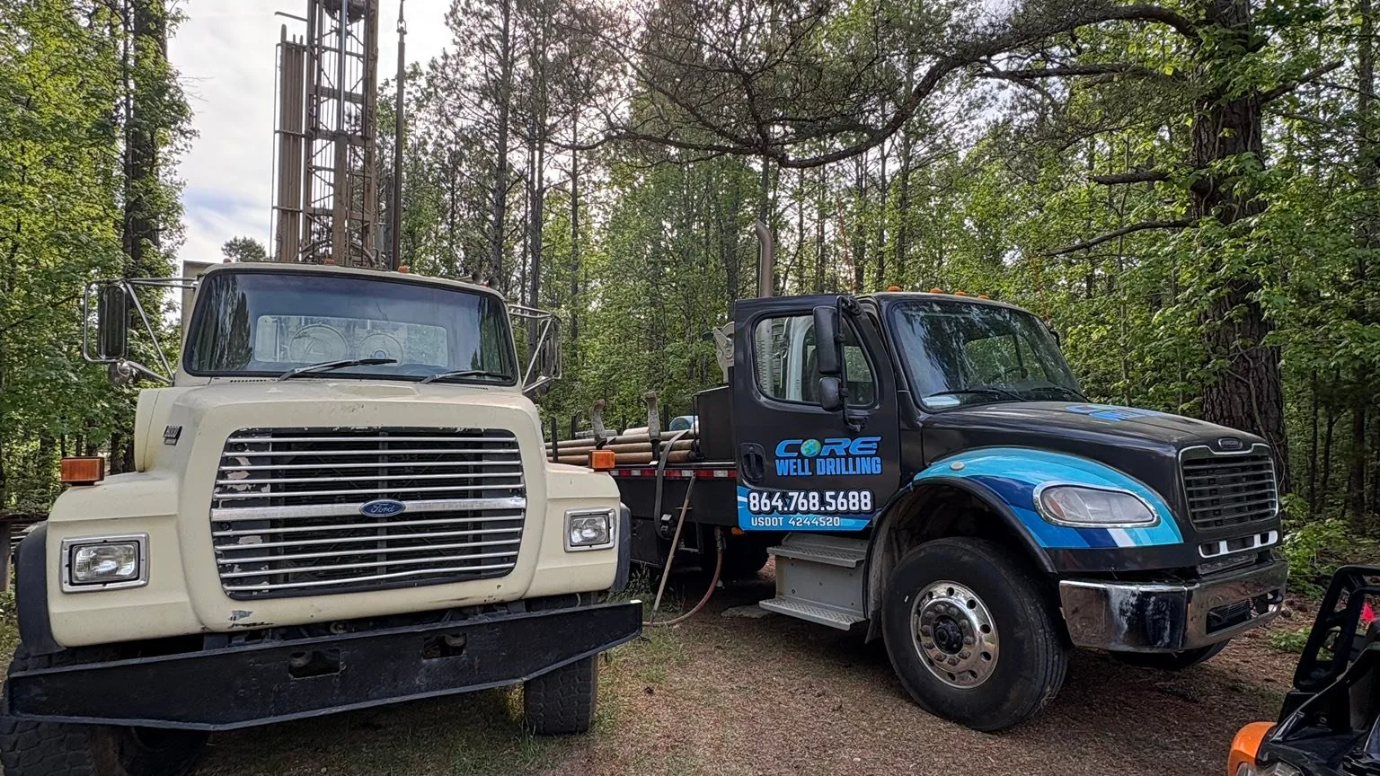 The water tank truck and the wrapped Core Well Drilling truck parked nose to nose on a wooded lane
