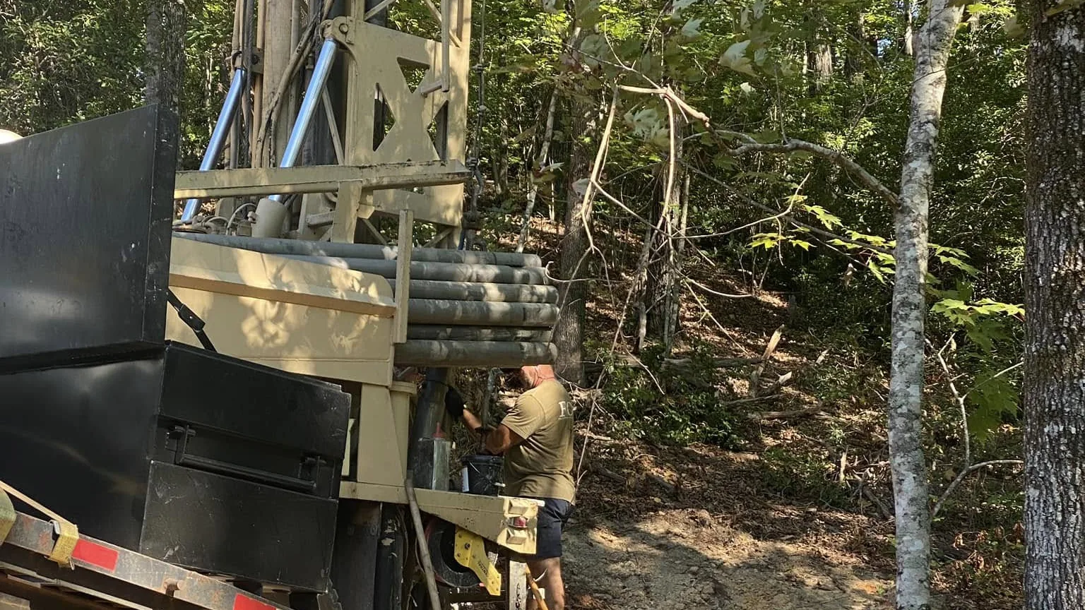 A crew member working at the drill rig on a steep rocky red clay site in the pines