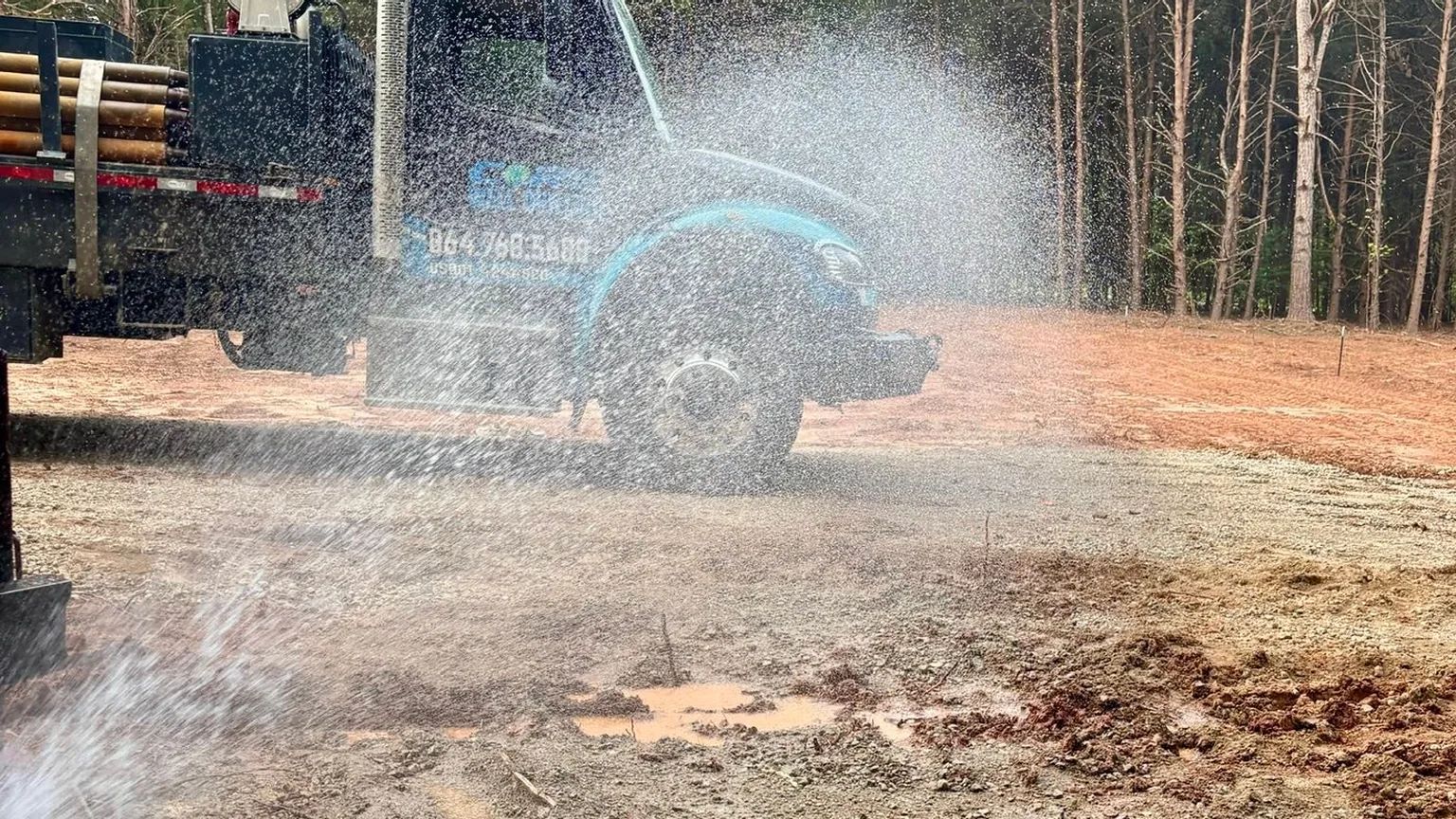 Water blowing out of a new well and spraying across the red clay past the company's service truck