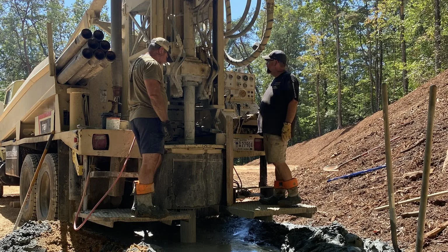 A drill rig boring a new water well with drilling water running off across the red clay
