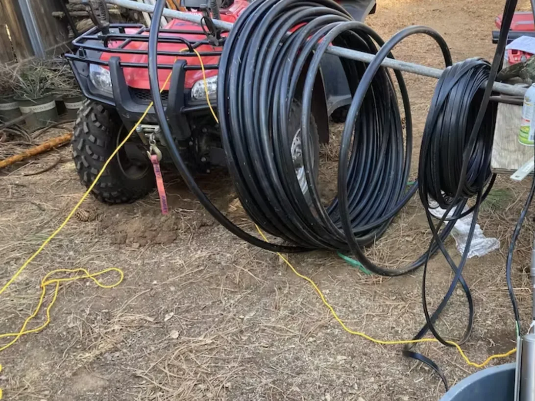 A submersible pump spliced to black poly drop pipe with the coil laid out, ready to be lowered into a well