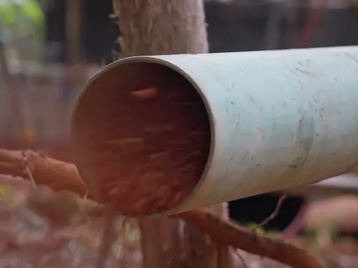 Water and drilling mud pouring out of the open end of a large well casing pipe on a wooded site