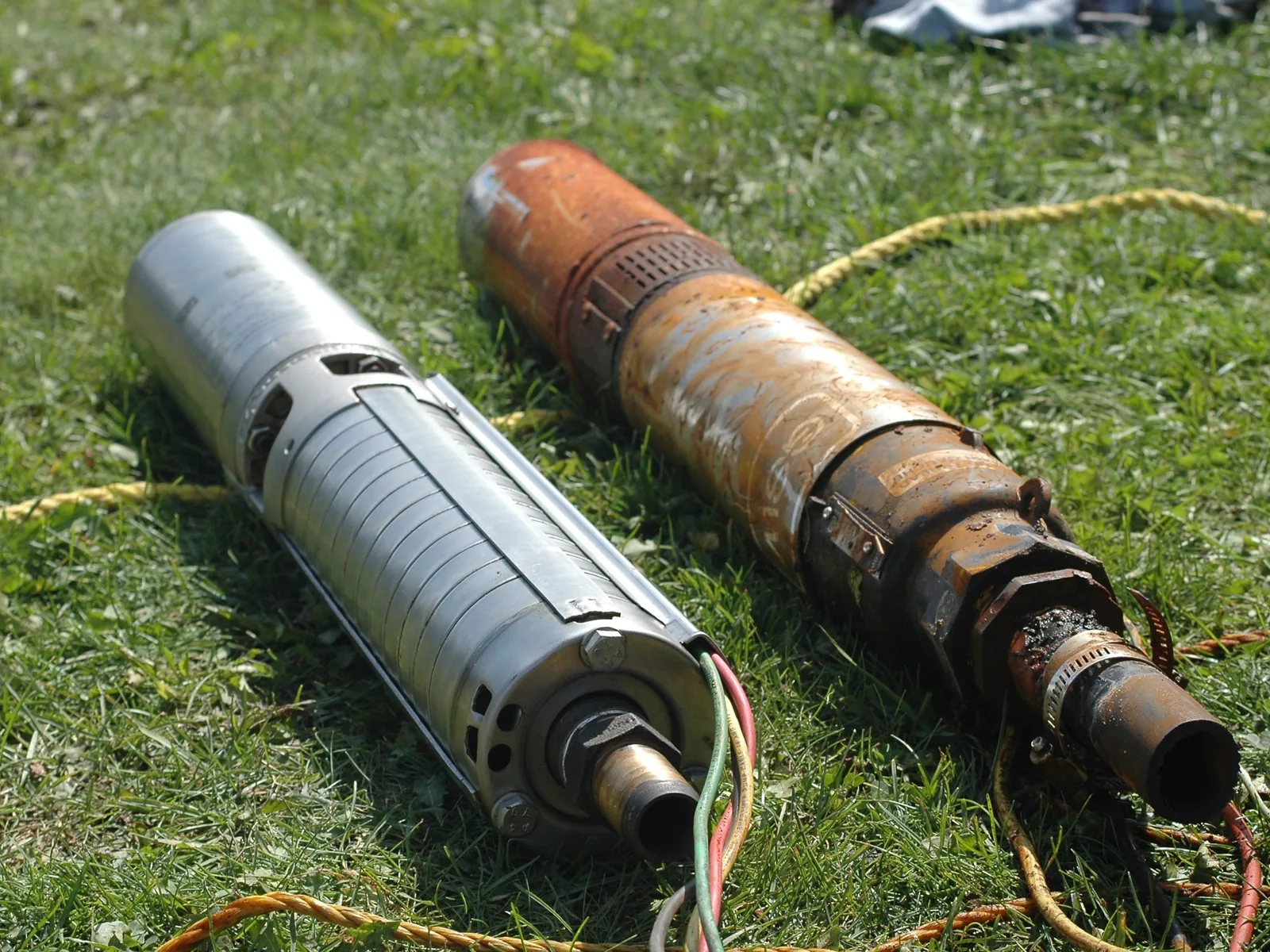 A new stainless submersible well pump lying on the grass next to the corroded pump it replaced